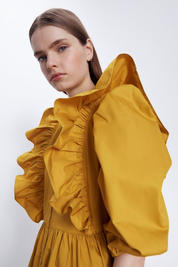 Vestido corto de cuello solapa y manga por debajo del codo abullonada acabada en elástico. Bolsillos laterales ocultos en costura. Detalle de volantes y pliegues. Cierre delantero con botones.