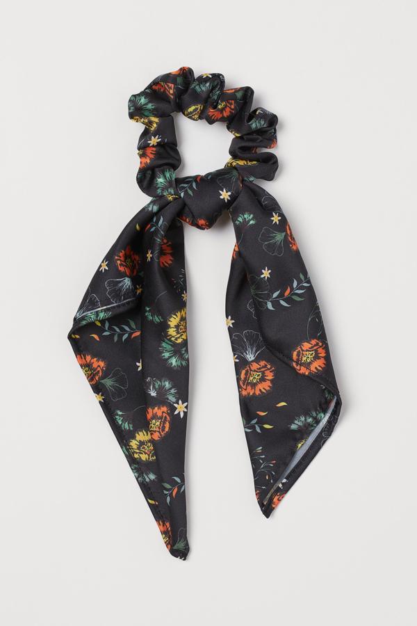 Sobre fondo negro con flores naranjas y amarillas, este coletero con lazada es de H&M y cuesta 4,99 euros. Solo está disponible en la web.