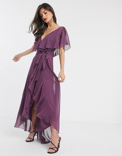 El tono ciruela se cuela en la lista con este favorecedor  vestido largo con bajo asimétrico  espalda tipo capa, escote a pico y cinturón ajustable. (57,99 euros).