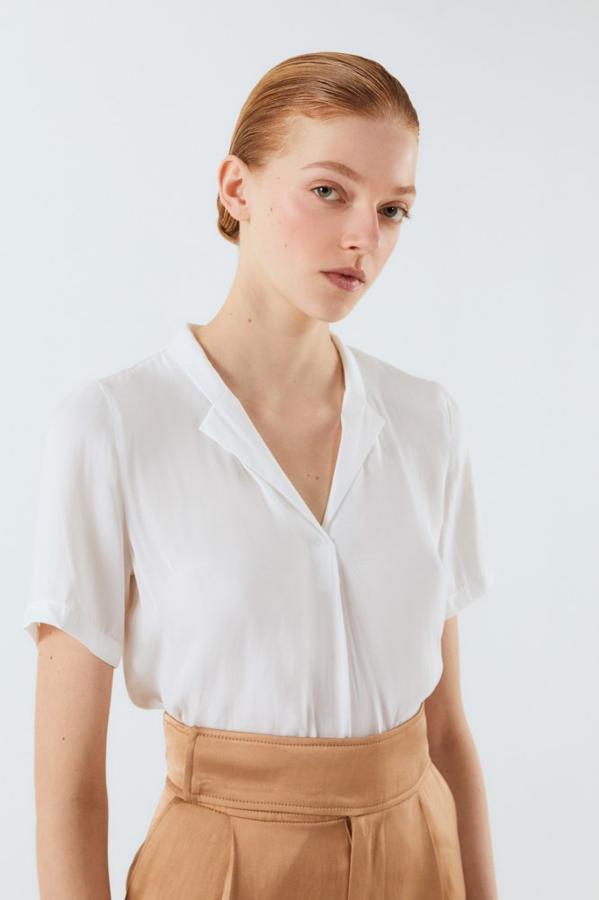 En Sfera hemos encontrado esta bonita blusa con cuello camillero y manga corta. Está disponible entre las tallas S y XL y cuesta 13,99 euros.