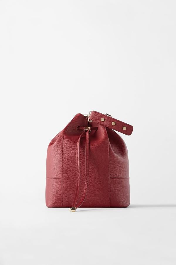 Con acabado abatanado y metales dorados, este bolso de Zara en color rojo tiene asa de mano y asa de hombro, ambas extraíbles. Cuesta 19,95 euros y también está disponible en negro.
