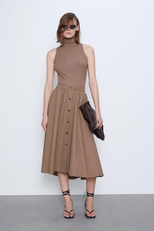 Con cintura elástica y bolsillos delanteros, esta falda midi capa de Zara en camel oscuro es una de nuestras favoritas. Con cierre frontal con botones metálicos a presión, cuesta 25,95 euros y está disponible entre las tallas XS y XL.