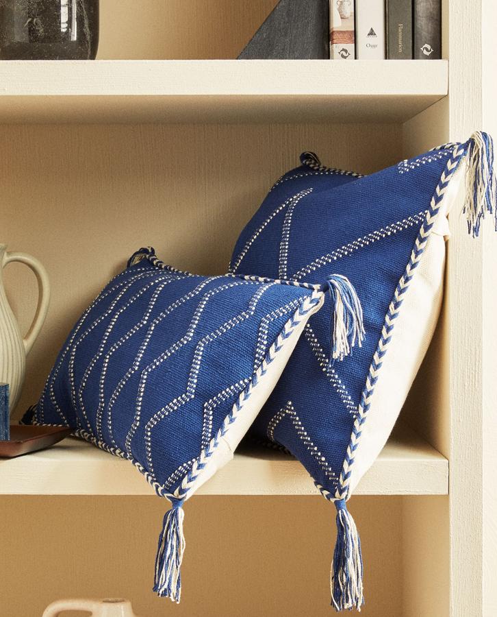 En tonos azul y blanco y rematado con pompones, esta funda de cojín de 30 x 50 centímetros cuenta con un dibujo en forma de zigzag y tiene un cierre con cremallera. Cuesta 19,99 euros.