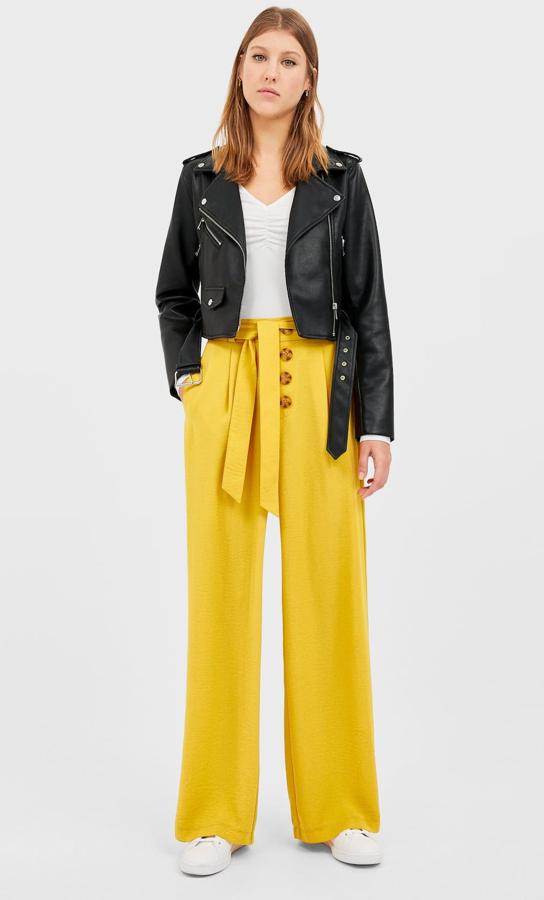 En tu armario no puede faltar un pantalón palazzo como este. En color amarillo, cuenta con botones y lazada a la cintura. Es de Stradivarius y tiene un precio de 13,99 euros.
