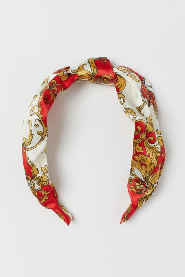 Estampado dorado y rojo sobre fondo blanco para esta diadema de H&M y acabado satinado. Tiene un precio de 7,99 euros.