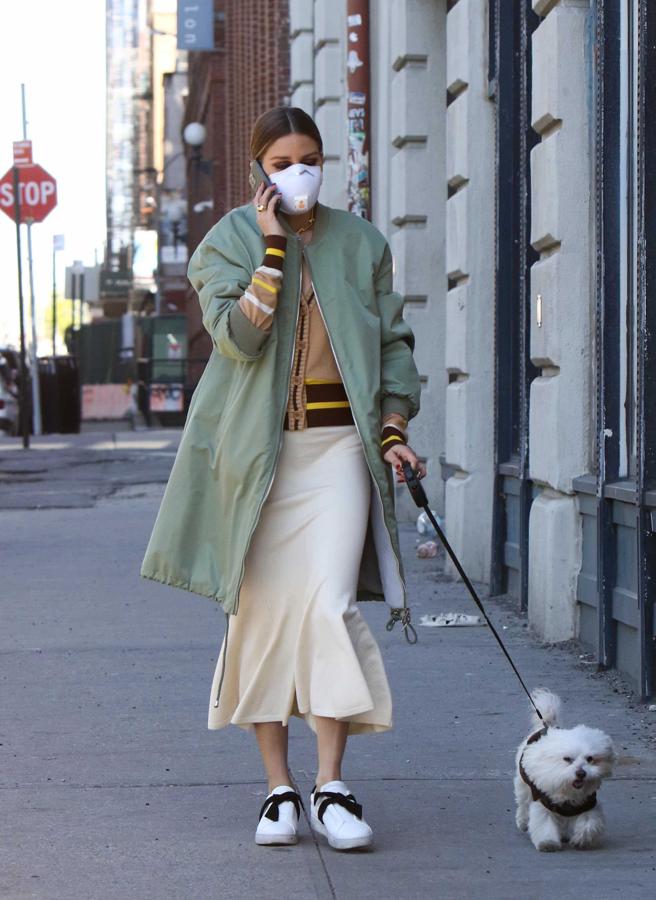 Con un abrigo estilo bómber militar extralargo sobre una rebeca beige y una falda midi con vuelo.