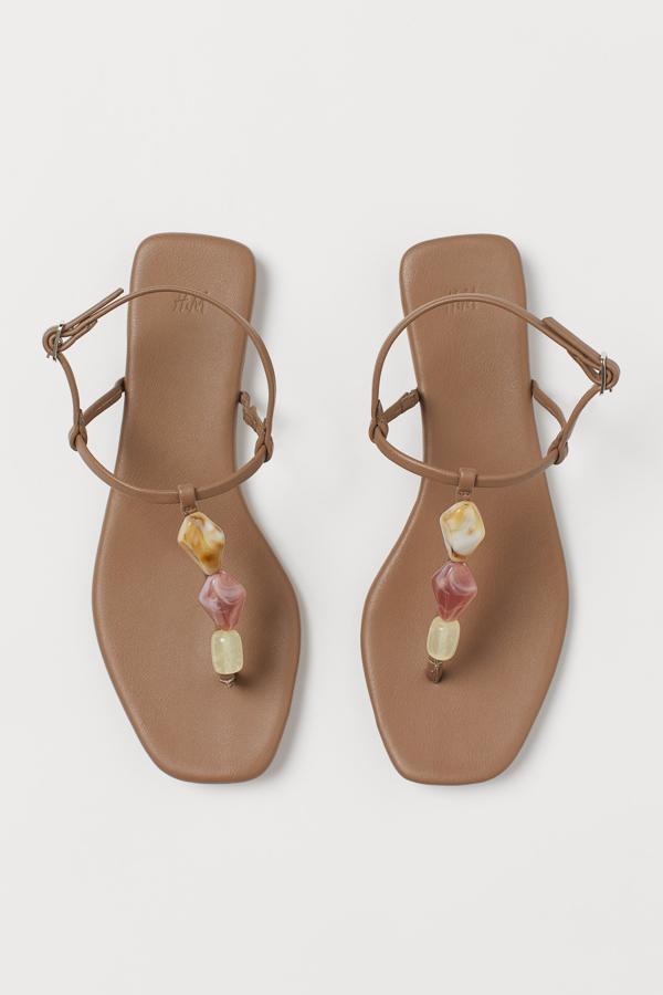 Con adornos de pedrería de plástico en el empeine y pulsera ajustable en el tobillo, estas sandalias planas en color marrón tienen un precio de 24,99 euros.