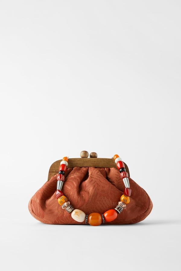 En color naranja, este bolso bandolera de tejido jaspeado con detalles florales y asa de mano extraíble con abalorios multicolor tiene un precio de 35,95 euros. También cuenta con asa de hombro con cadena dorada.