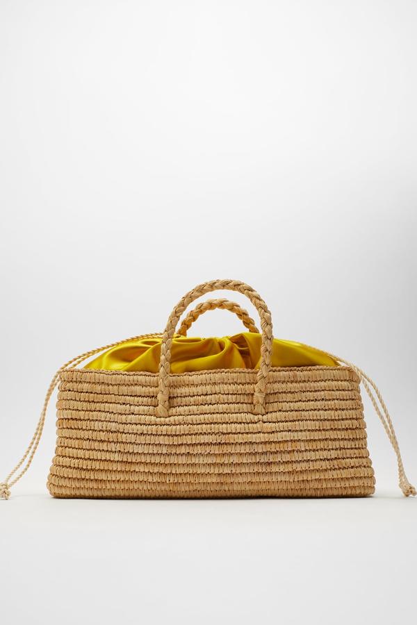 En color natural, este bolso en formato cesta con cuerpo trenzado de rafia cuenta con asa de mano y bolsa interior de tejido satinado en amarillo. Tiene un precio de 29,95 euros.