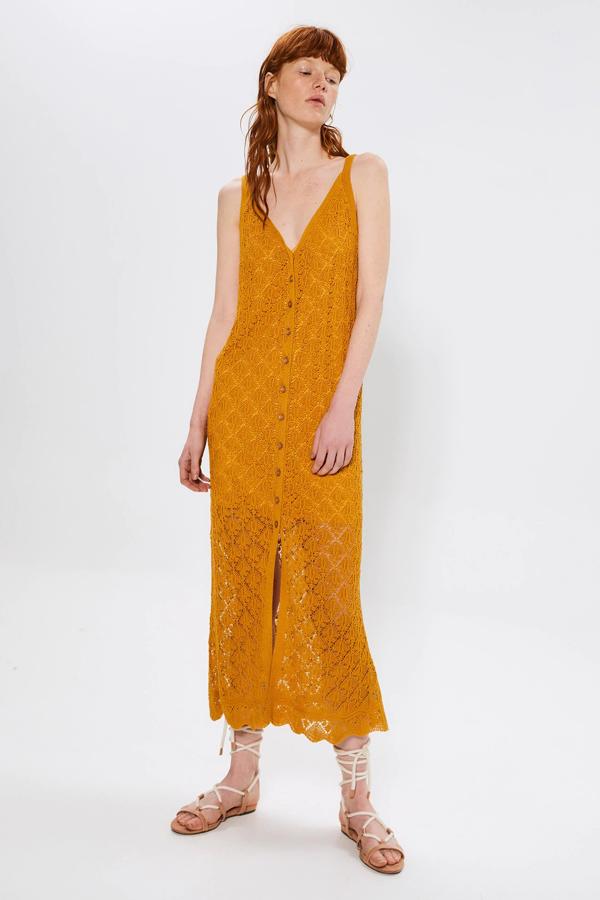 Este vestido largo de punto en crochet con cuello de pico y tirantes, cuenta con detalle de volantes en la parte delantera. En color mostaza, es de Sfera y está rebajado a 23,99 euros.