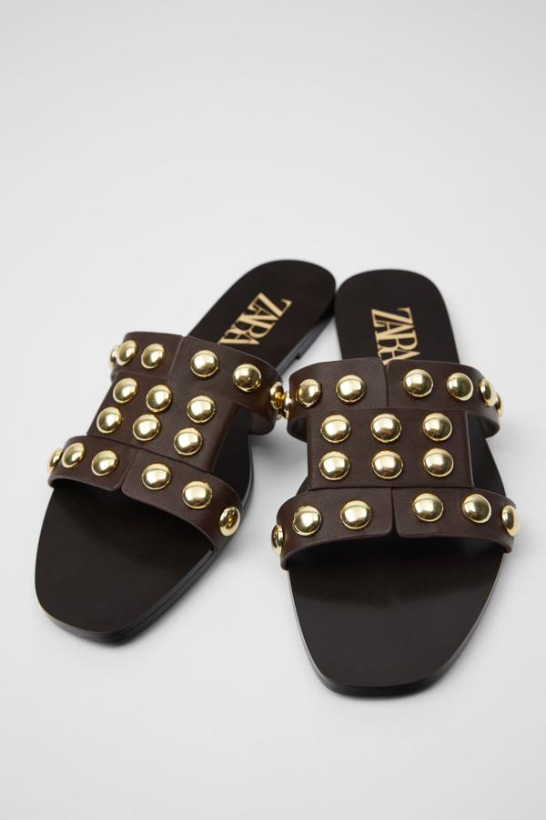 En color marrón, estas sandalias planas de piel con detalle de tachas en dorado en la parte delantera son de Zara y tienen un precio de 29,95 euros.