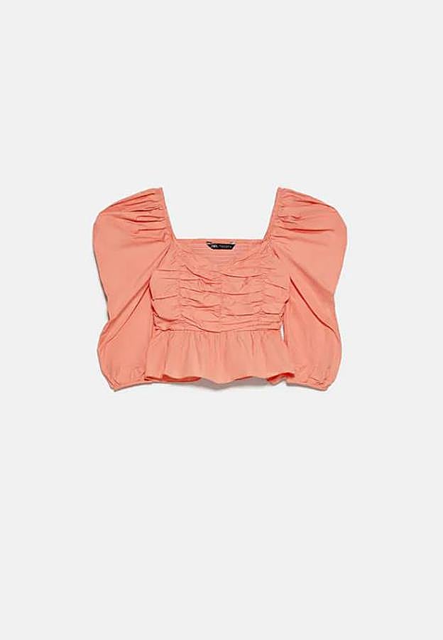 No es la primera temporada que nos topamos con tops de escote pico amplio, manga por debajo del codo abullonada y detalle de frunces como este. Pero nos siguen conquistando y el coral es uno de los colores más favorecedores para el verano. Cuesta 25,95 euros.
