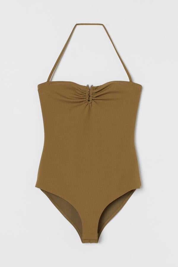 Body en punto de crepé con adorno con forma de U en la parte superior. Es de color caqui y lleva una tira de quita y pon en la nuca, borde de silicona oculto en la parte superior y botones de presión en la entrepierna (H&M, 24,99 euros).