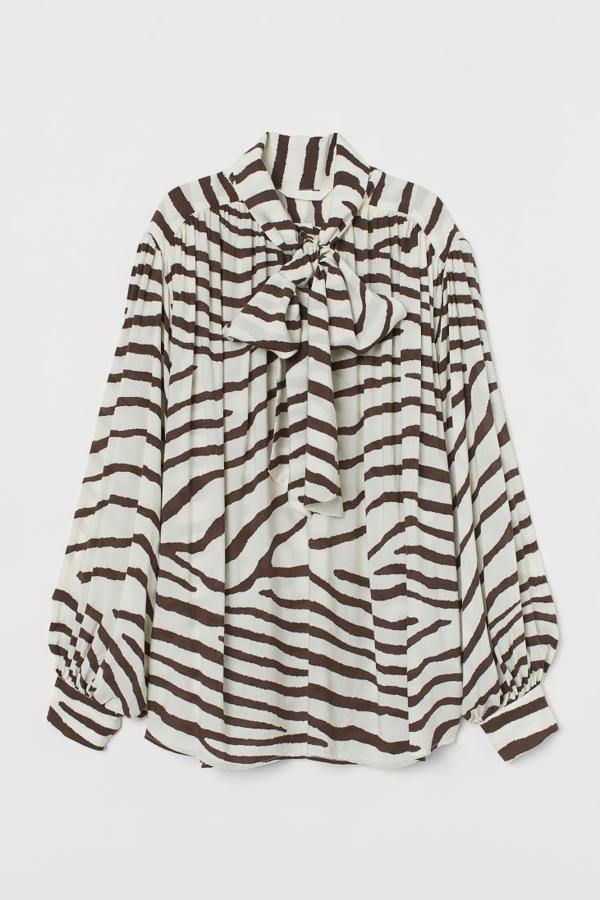 Blusa estampada de corte holgado en tejido vaporoso de viscosa (29,99 euros). Lleva cuello ancho con lazo grande, tapeta de botones, mangas largas amplias con botón revestido en los puños y canesú fruncido en hombros y espalda.