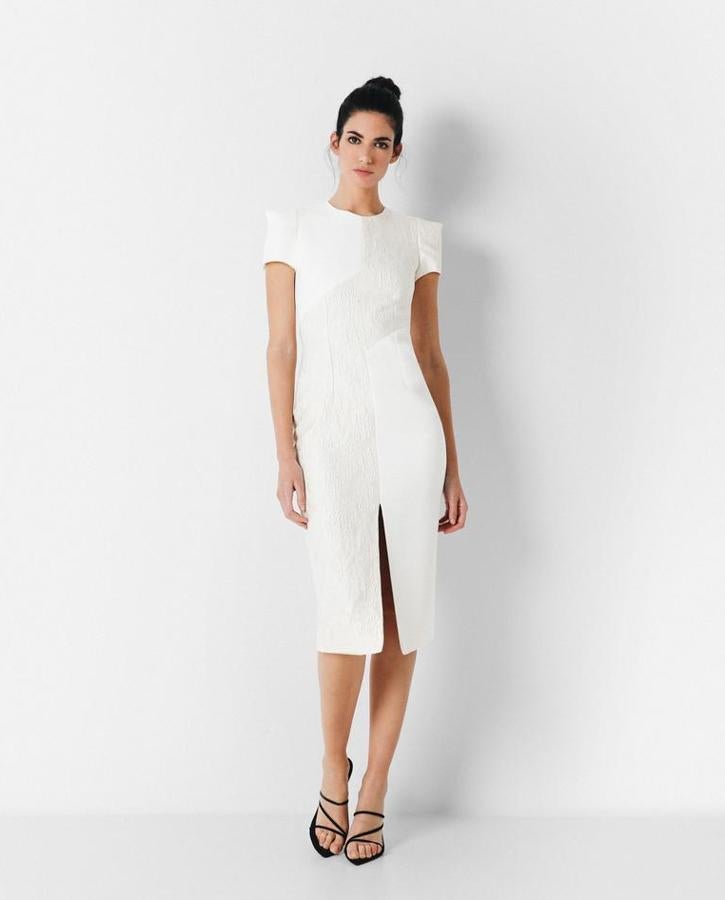 Vestido de invitada beige de corte midi con escote a la caja y manga corta. El crepé del vestido está mitad brocado y mitad liso que aportan inevitablemente un toque vintage. La abertura en el bajo del centro delantero del vestido aportan fluidez y comodidad al look. Rebajado de 215 euros a 150 euros.