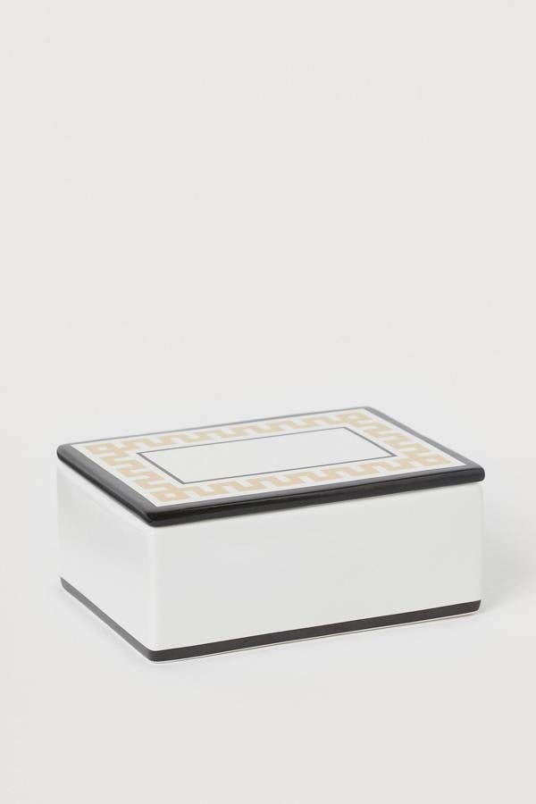 Esta caja rectangular de porcelana en color blanco con adornos en negro y dorado cuenta con tapa a juego. Con una altura de 6 centímetros, un ancho de 10,5 y un largo de 14,5, tiene un precio de 10,99 euros.