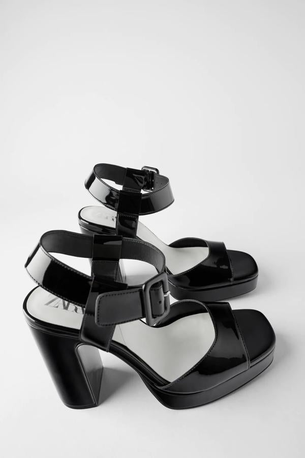 A pesar de sus 12 centímetros de tacón, esta sandalia resulta de lo más cómoda por su plataforma. En color negro con efecto charol, cuenta con tira en la parte delantera y cierre mediante hebilla en pulsera al tobillo. Forma parte de las rebajas de Zara y tiene un precio de 19,99 euros.