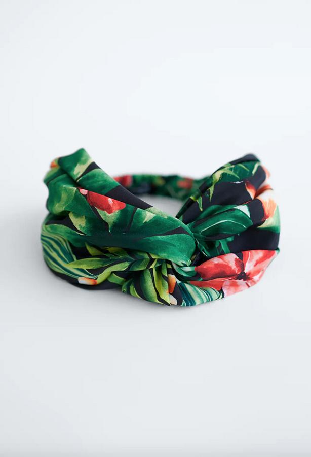 Fondo negro con vistoso estampado de flores y hojas en tonos rojos y verdes para esta diadema turbante de Zara que tiene un precio de 7,95 euros.