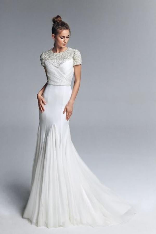 Vestido de novia realizado en crepe velado en tul seda, con escote a la caja y manga corta realizado en pedrería en degradé, drapeado de tul seda realizado sobre el cuerpo y falda vuelo de godet de tul seda. Rebajado de 1.990 a 796 euros.