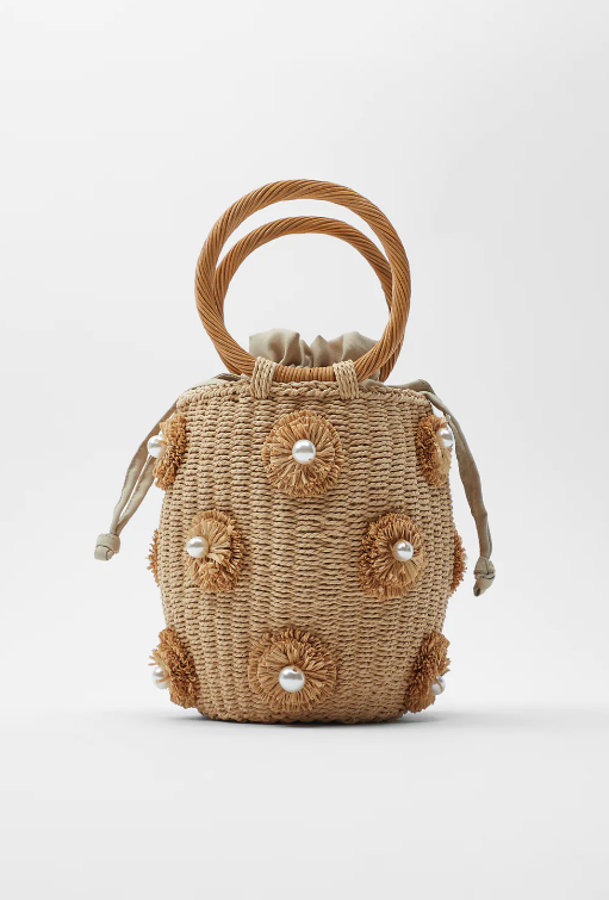 Otro complemento confeccionado con materiales naturales que la da el toque de tendencia de temporada a cualquier estilismo. Se trata de un bolso formato cesta con el cuerpo trenzado, una decoración con perlas y asas circulares (Zara, 35,95 euros).