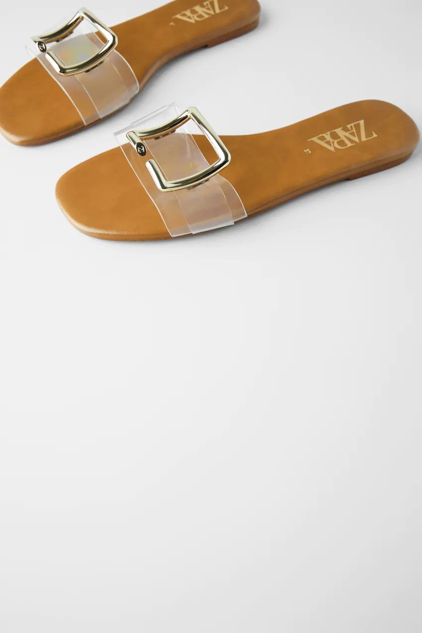 Diseño de vinilo con pieza metálica de Zara. Unas sandalias planas que son pura tendencia y que alargan las piernas gracias a su efecto invisible con el que ganar unos centímetros. Ahora: 15,99 euros.