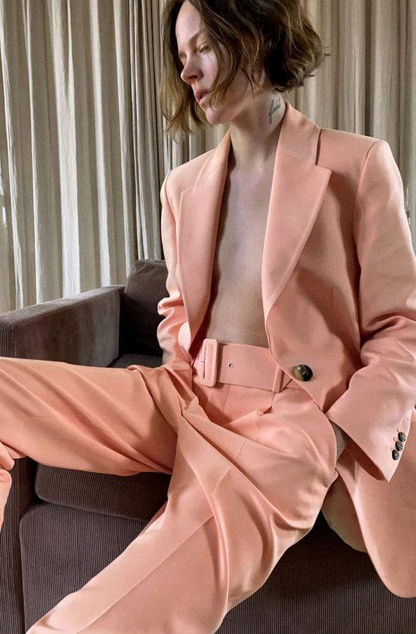En un bonito color melocotón, este traje de Zara está compuesto por una blazer de cuello y solapa con manga larga con cierre frontal de botones a contraste (49,95 euros) y un pantalón de tiro alto con cinturón forrado a tono (29,95 euros).
