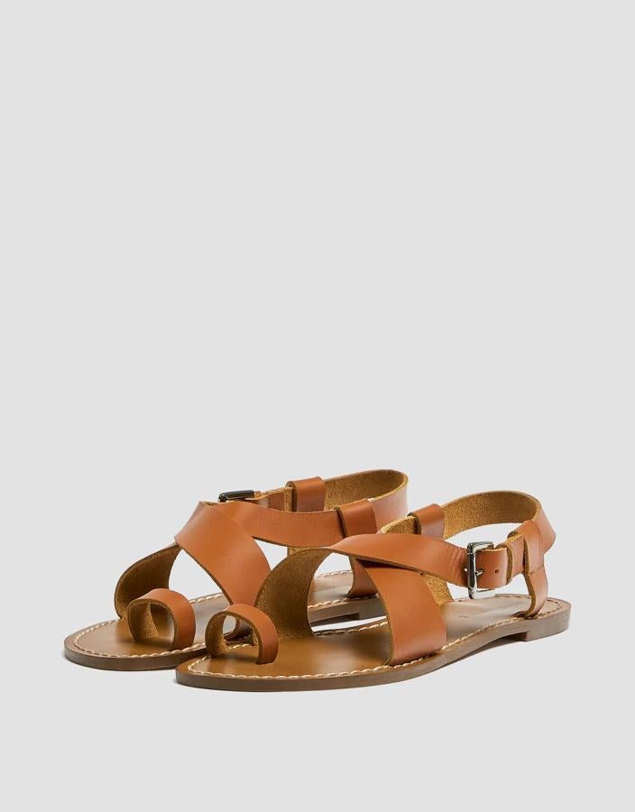 Esta sandalia plana de cuero en color natural cuenta con cierre mediante hebilla lateral y detalle de tiras cruzadas. Está rebajada y tiene ahora un precio de 15,99 euros.