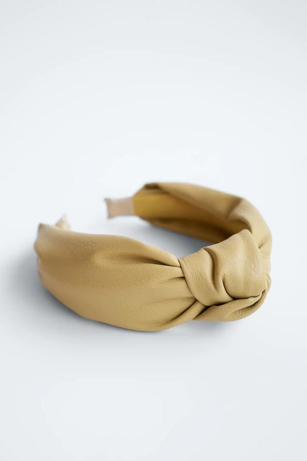 Disponible en tono oliva o negro, esta diadema de efecto piel con detalle de nudo es de Zara y tiene un precio de 9,95 euros.