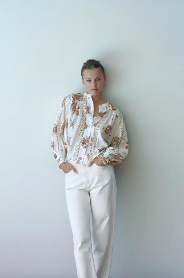 De cuello redondo y manga larga abullonada, esta blusa de Zara con detalles de encaje combinados en color crudo viene con un bonito estampado de flores en tonos rojos y verdes. Tiene un precio de 29,95 euros y está disponible entre las tallas XS y XXL.