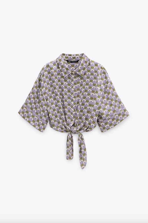 Diseño corto para esta camisa de cuello solapa y manga corta con detalle de nudo en el bajo y cierre frontal con botones. Con un estampado en tonos verdes y lilas, tiene un precio de 22,95 euros y está disponible entre las tallas XS y XXL.