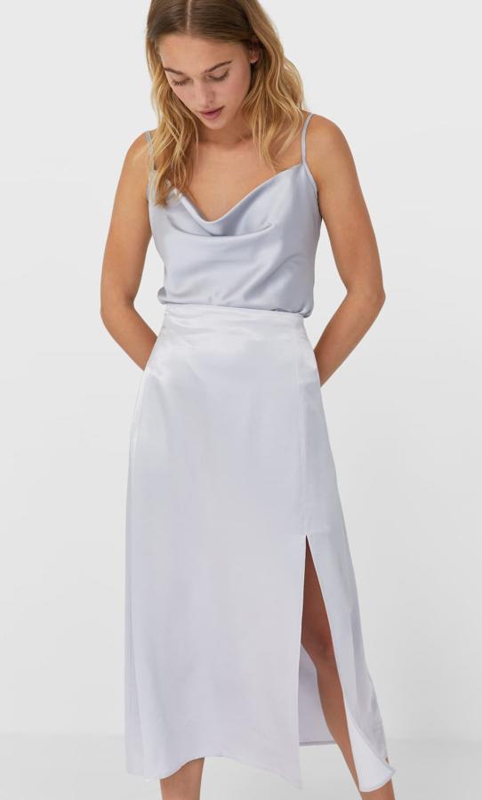 En Stradivarius también han apostado por las aberturas y una de las propuestas más atractivas es esta falda midi de tiro alto con cintura elástica en la espalda y bajo con abertura en delantero. En color gris perla, podemos encontrarla entre las tallas XS y XL por 17,99 euros.