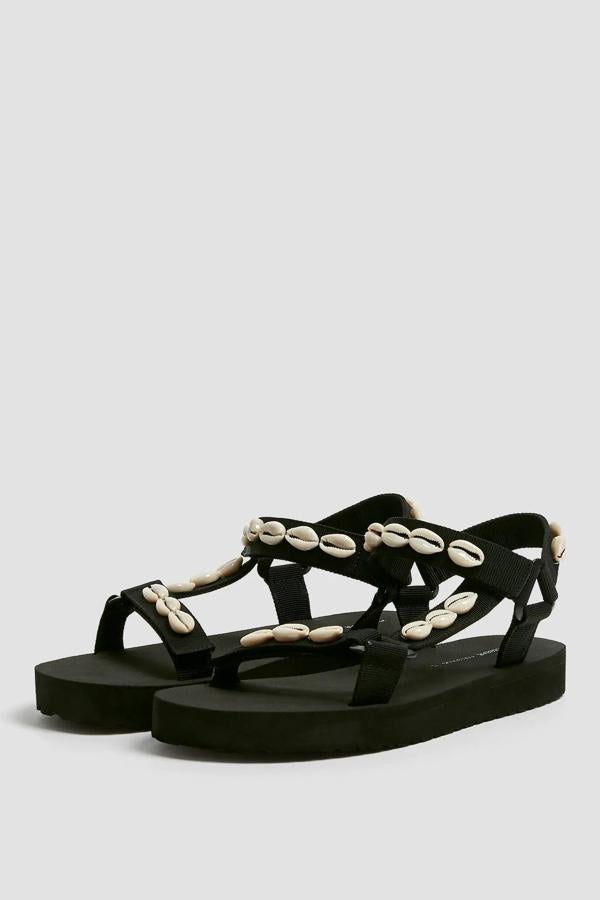 Esta sandalia plana en color negro con detalle de conchas cuenta con cierre en la parte trasera mediante cinta adherente. Es de Pull & Bear y tiene un precio de 29,99 euros.