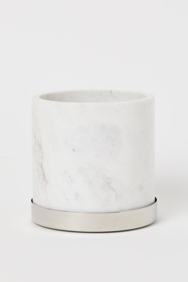 De mármol blanco y con platillo plateado, esta maceta con agujero de drenaje y una altura aproximada de 15 centímetros es de H&M Home y tiene un precio de 39,99 euros.
