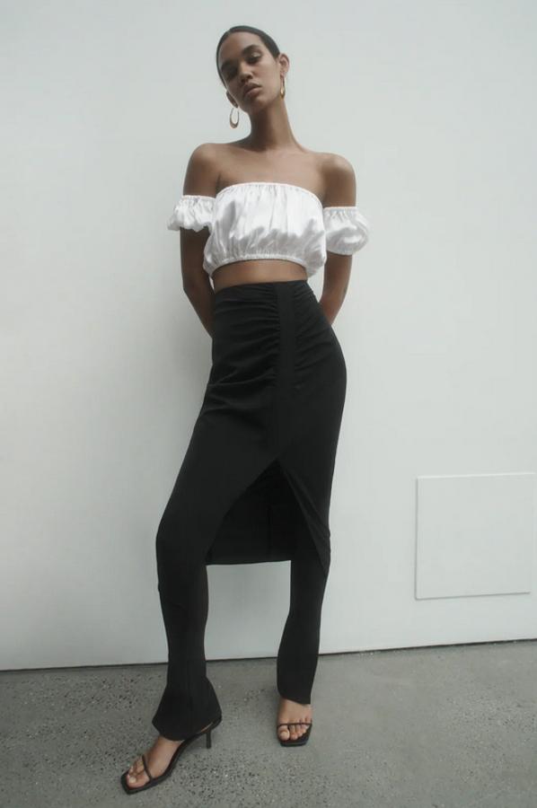 En Zara hemos encontrado esta falda midi con frunces delanteros y bajo con abertura frontal. En color negro, cuesta 25,95 euros y está disponible entre las tallas XS y XL.
