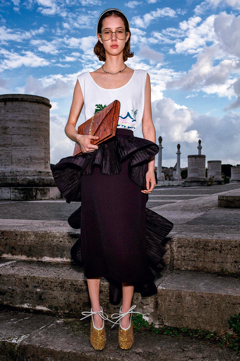 Camiseta de tirantes estampada, falda de crepé con volante plisado, diadema de strass, gafas, gargantilla de plata, cartera de mano en pitón y botines de lentejuelas, todo de Gucci.