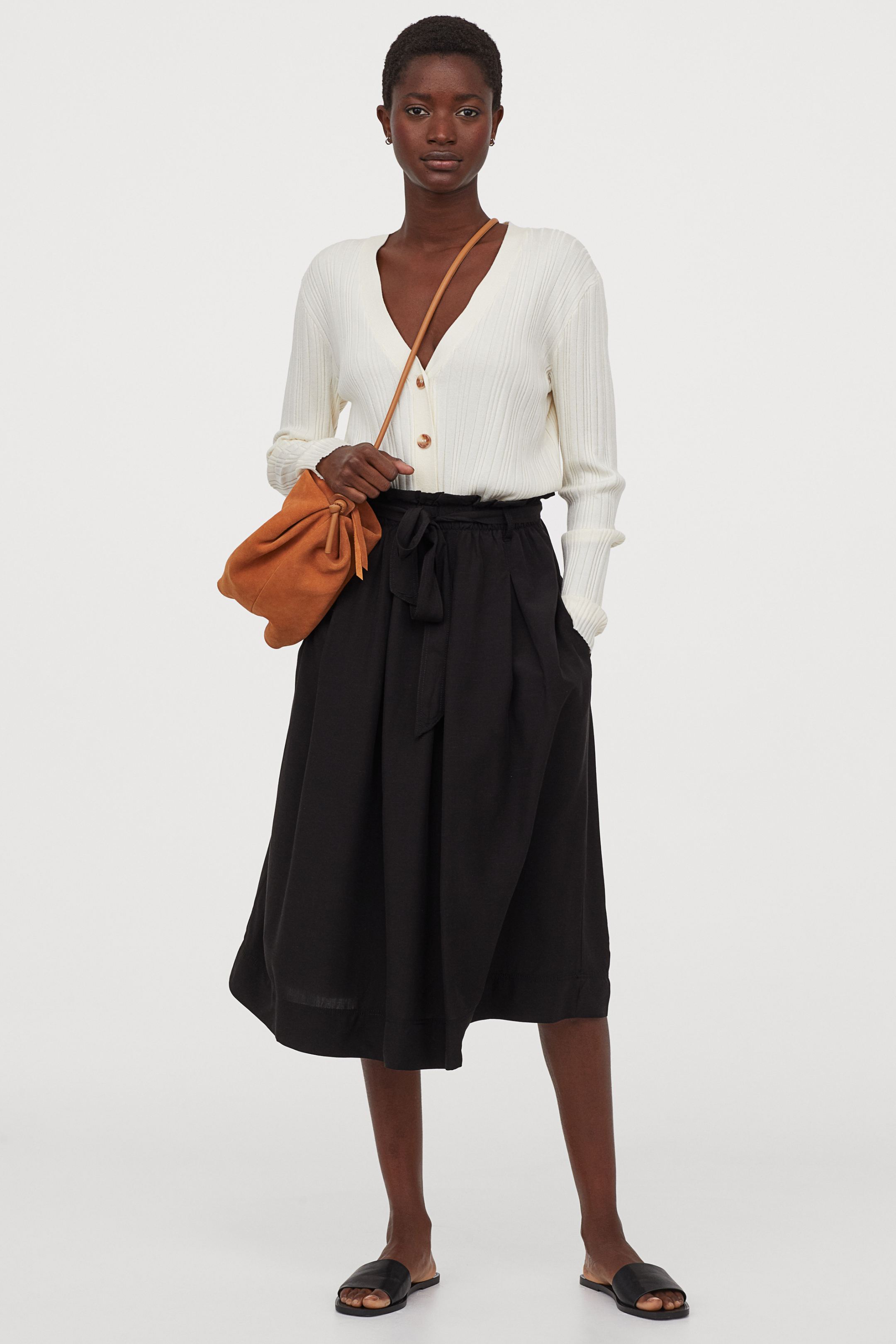 Un básico perfecto para solucionar cualquier estilismo de entretiempo: la falda fluida con cinturón en color negra, la más versátil. De la nueva colección de H&M. (29,99 euros).