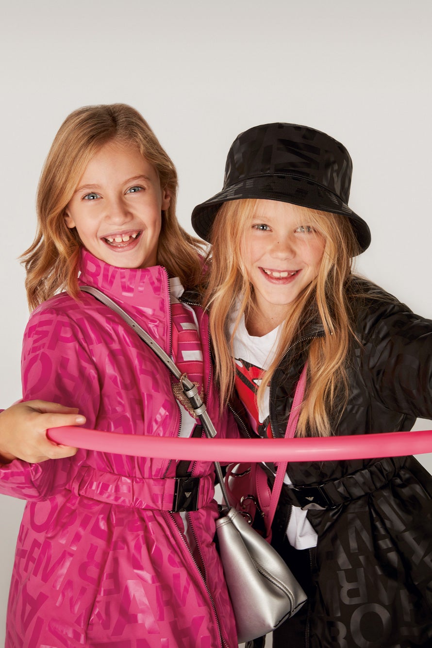 A la izda., gabardina rosa, camiseta y bolso plateado. A la dcha., gabardina negra, camiseta gorro y bolso rosa. Todo de Emporio Armani.