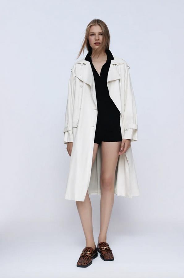 Tejido water repellent en efecto piel para esta gabardina en color crudo de Zara con mangas largas acabadas en trabilla, bolsillos laterales con solapa y cinturón con hebilla forrada en el mismo tejido. Solo podemos encontrarla en la talla M por 69,95 euros.