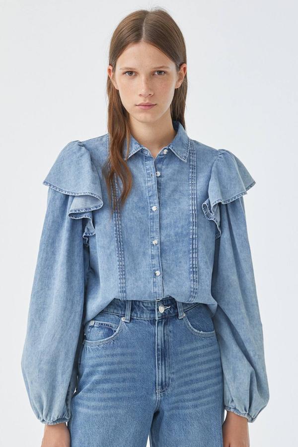 Esta camisa denim con detalle de volante en el hombro cuenta con goma en los puños y cierre mediante botones. Está confeccionado en 100% algodón y tiene un precio de 25,99 euros.