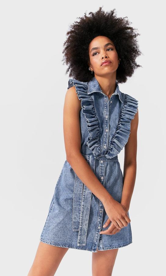 En denim claro, este vestido corto con detalle de volantes en la parte delantera cuenta con cinturón del mismo tejido y cierre frontal con botones. Tiene un precio rebajado de 20,99 euros.