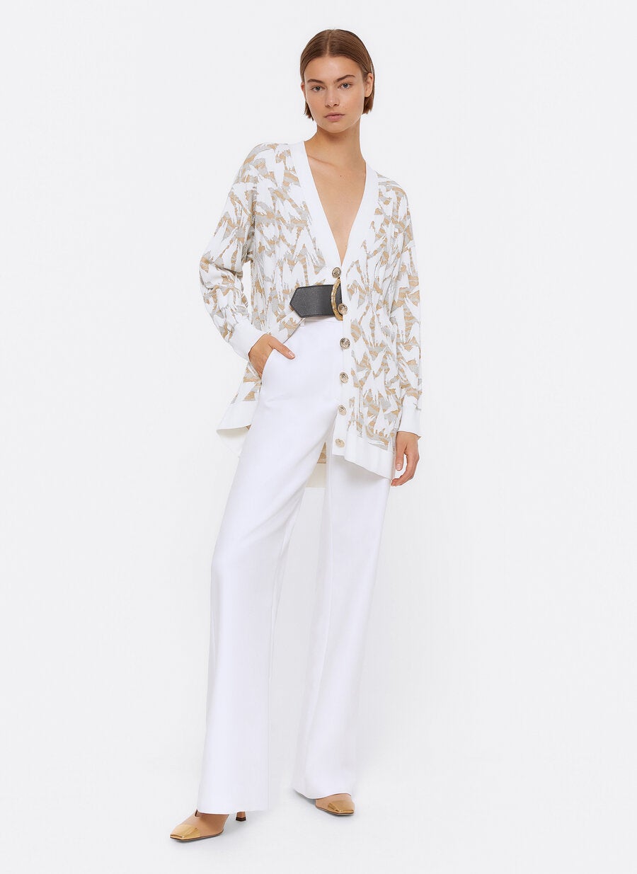 Cárdigan blanco de punto jacquard con estampado geométrico de hilo metalizado, escote a pico y botones dorados. (99 euros).