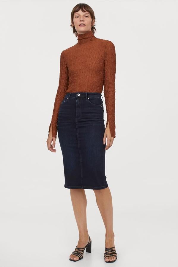 En denim lavado en negro azulado, esta falda de cinco bolsillos con strech técnico que sujeta y moldea la cintura tiene el talle alto y abertura trasera en el bajo. Es de H&M, cuesta 29,99 euros y está disponible entre las tallas 32 y 48 y en color negro.