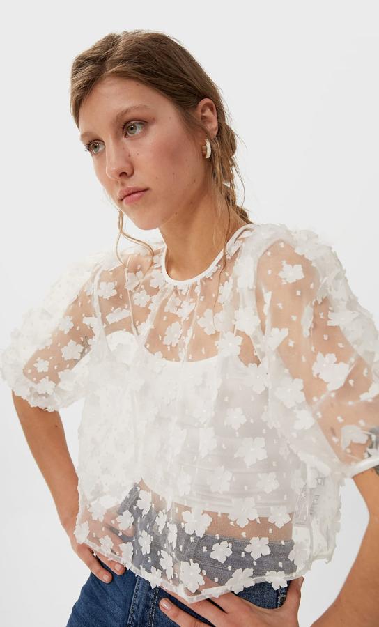 Diseño semitransparente con cuello redondo y manga corta abullonada para esta blusa de organza de Stradivarius en color blanco con detalle de flores con relieve. Tiene un precio de 25,99 euros y está disponible únicamente en la talla L.