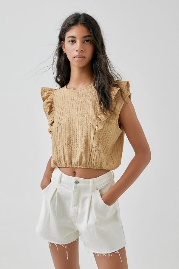 En color café o malva, este top corto de cuello redondo y manga sisa cuenta con detalle de volantes y goma en el bajo. Tiene un precio de 9,99 euros.