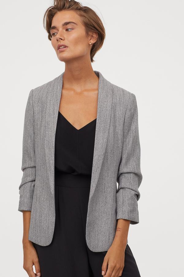 Disponible en varios colores, esta americana en gris jaspeado cuenta con cuello smoking, manga tres cuartos con costuras fruncidas y bolsillos en las costuras laterales. No tiene cierre, es de H&M y tiene un precio de 39,99 euros.