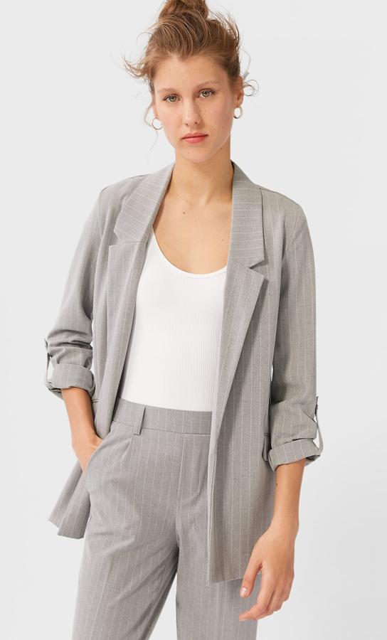 Esta blazer fluida en color gris con raya fina cuenta con manga por debajo del codo acabada en vuelta con trabilla y falso botón metálico. Es de Stradivarius y tiene un precio de 25,99 euros.