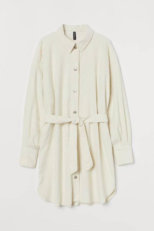 Color crema para este vestido corto de algodón con cuello camisero, bolsillo de tapeta en el pecho y cierre de botones vistos. De corte recto con hombros caídos, tiene las mangas largas con puños sencillos, cinturón a tono y bajos asimétricos redondeados. Tiene un precio de 29,99 euros y está disponible entre las tallas XS y XL.