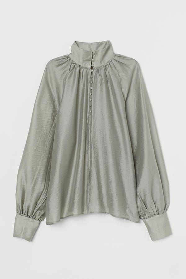 En color verde caqui (también está disponible en crema o negro), esta blusa en satén fluido con cuello elevado y mangas globo cuenta con pliegues fruncidos en el cuello y tiene un precio de 34,99 euros. Es de H&M.