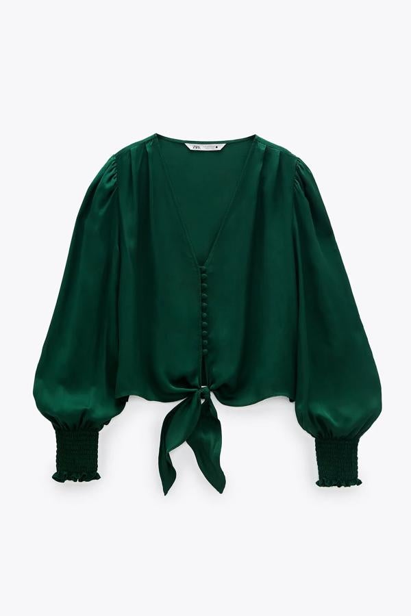 Esta blusa verde botella con escote de pico y manga larga acabada en puño elástico cuenta con un nudo en el bajo de la parte delantera y botones forrados. Es de Zara y tiene un precio de 25,95 euros.