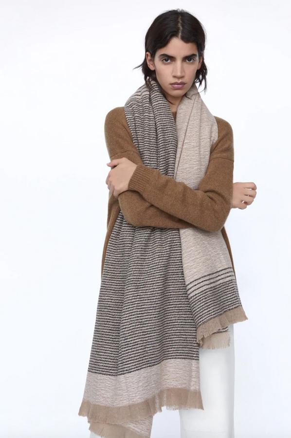 En tacto suave y acabado con flecos, este pañuelo en color tostado con rayas laterales en tonos grises es de Zara y cuesta 19,95 euros.